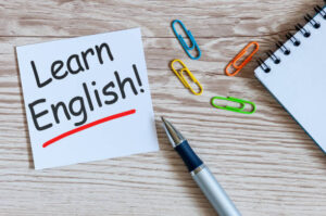 Learn english - note at wooden background with teachers glasses.